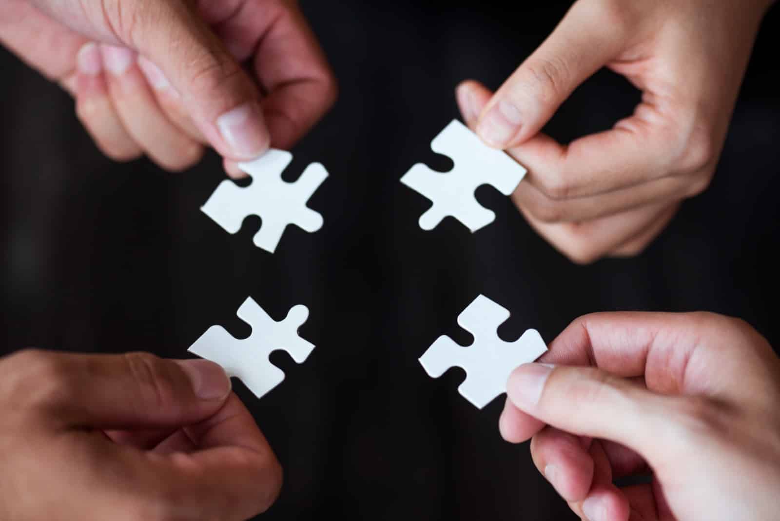 Four Hands Holding Puzzle Pieces Together