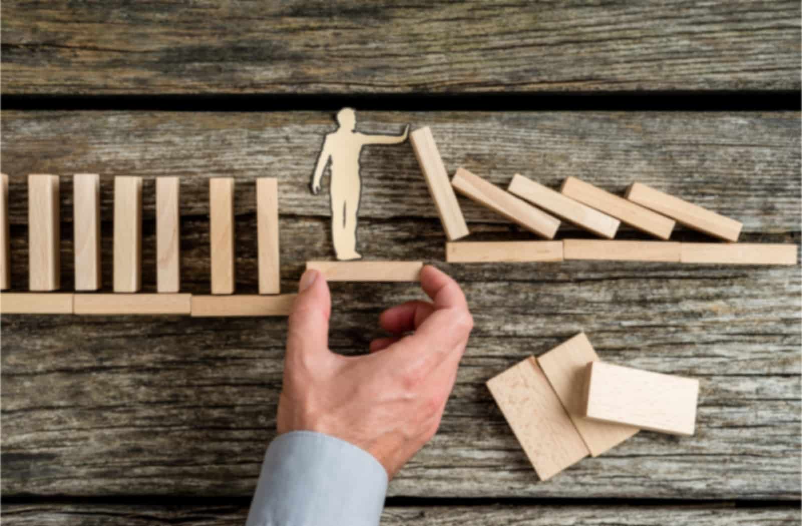 Hand Holding Up Wooden Figure That Is Blocking Dominoes