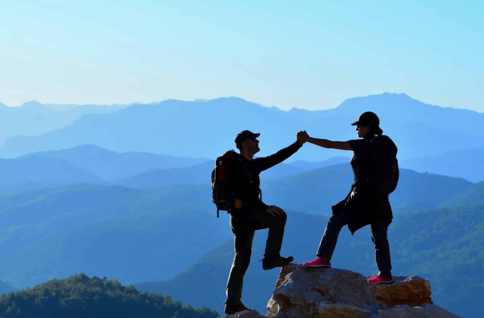 Hikers Holding Hands On High Rock With Mountain Background